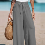 Person wearing gray wide-leg pants and a white top on a beach.