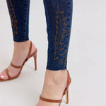 Close-up of blue jeans with embroidery and brown high-heeled sandals on a light gray background