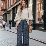 Woman in a stylish outfit with a white top and blue patterned pants walking on a city street.