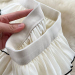 Close-up of a white dress with a belt being adjusted on a fluffy white background