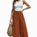 Person wearing rust-colored wide-leg pants and a white top on a beach.