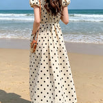 Woman in a polka dot dress standing on a beach with ocean view