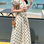 Woman in a polka dot dress holding a drink by the beach