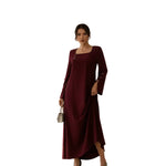 Woman wearing a burgundy dress with long sleeves against a white wooden panel background