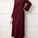 Woman wearing a burgundy long-sleeve dress against a white wall.