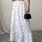 Person wearing a white skirt with black patterns and holding a black handbag.