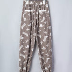 Brown pants with white pattern on a hanger against a light gray background