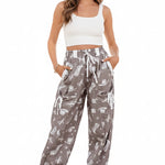 Person wearing gray patterned pants with a white top and sandals on a light background