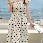 Woman in a polka dot dress by the sea holding a drink.