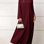 Woman wearing a burgundy long-sleeve dress with a white handbag against a light wooden background