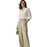 Person wearing a white shirt and beige wide-leg pants against a plain background